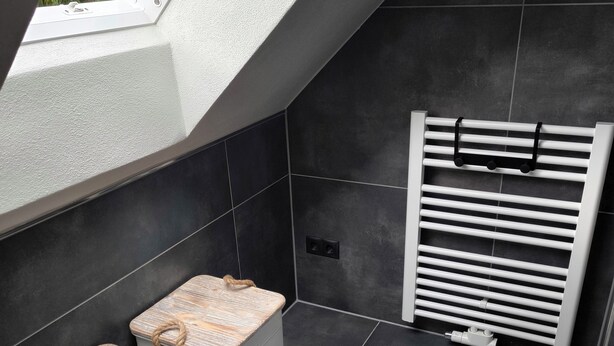 A modern bathroom with a skylight, two wooden stools, a towel rack, and a radiator. - Vacation home Oberwildenthal M.ORE MOUNTAINS CHALET 110sqm (Eibenstock)
