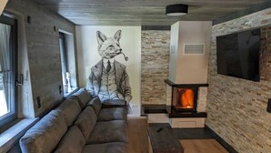 A modern living room with a large sectional sofa, a fireplace, and a stone wall. - Vacation home Oberwildenthal M.ORE MOUNTAINS CHALET 110sqm (Eibenstock)