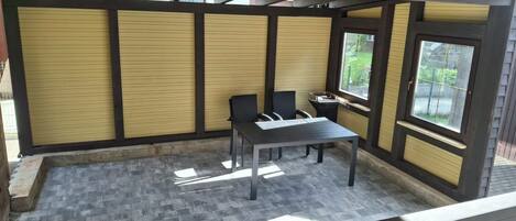 A covered patio area with a table and chairs, a window, and a door.