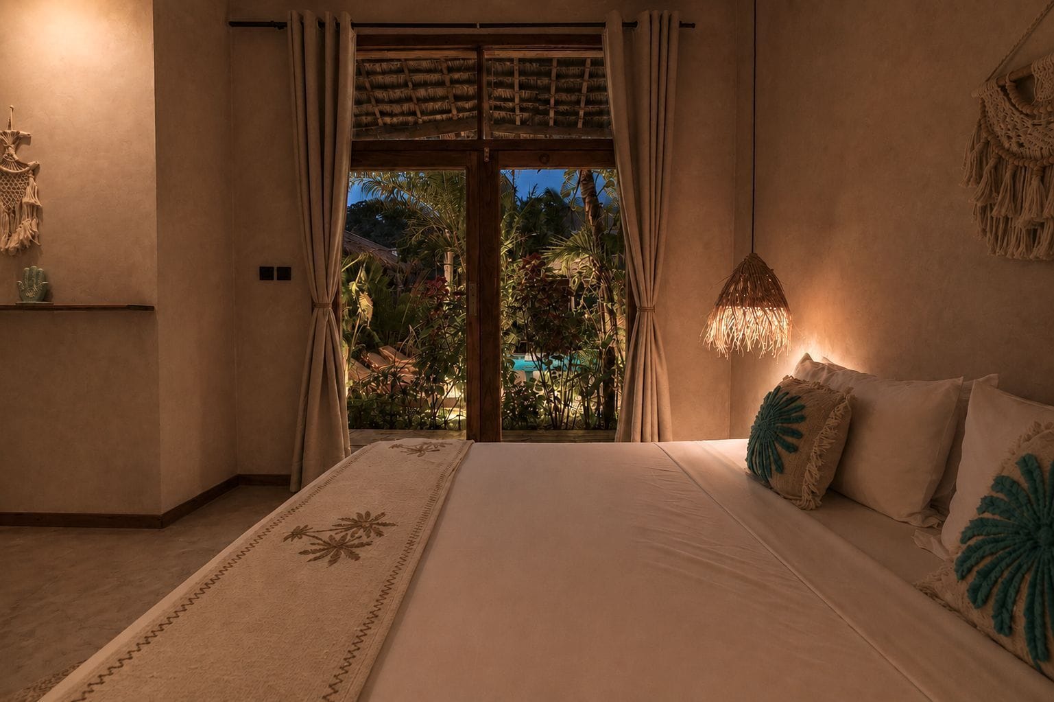 Una camera da letto con un letto, un comodino, un arazzo macramè e vista su un giardino attraverso una porta vetrata.