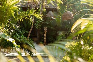 A tropical garden with a thatched-roof structure, a pathway, and a signpost with numbers.