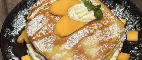 A stack of pancakes with syrup, whipped cream, and a mint leaf on a black plate.