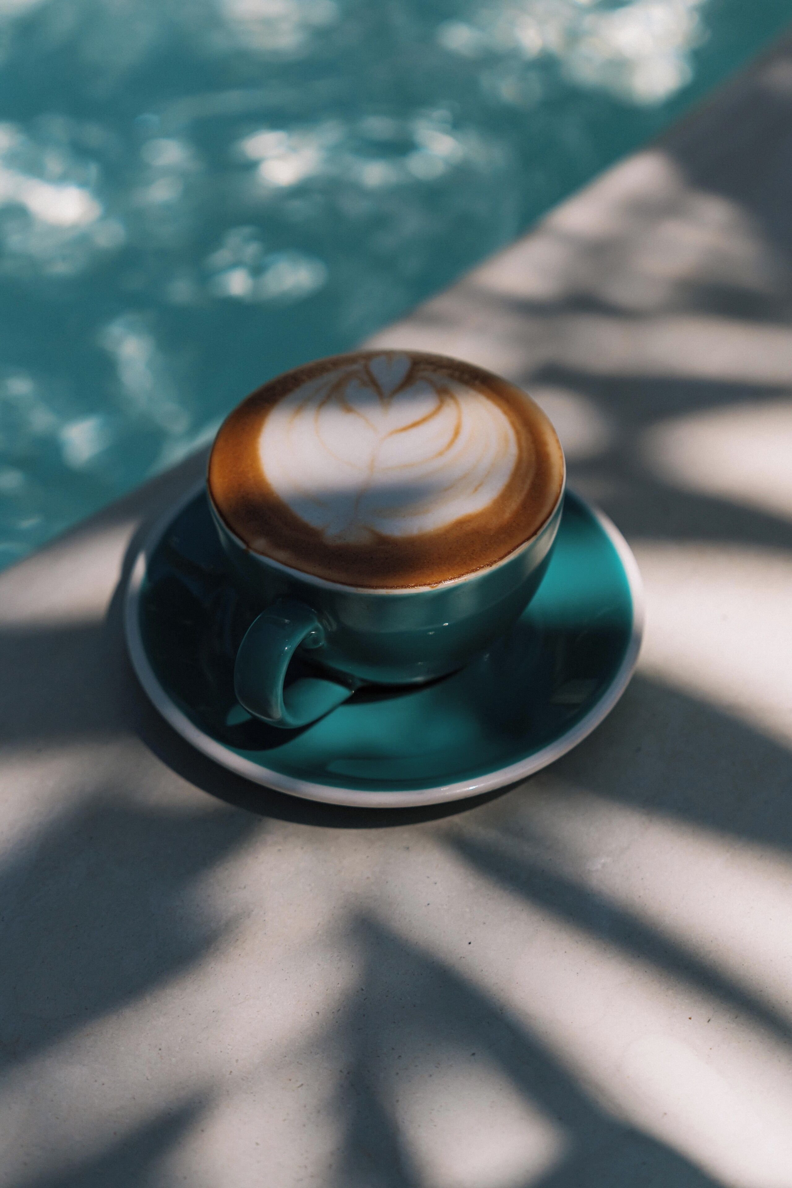 Een kop koffie met latte-art op een schotel, bij een zwembad.
