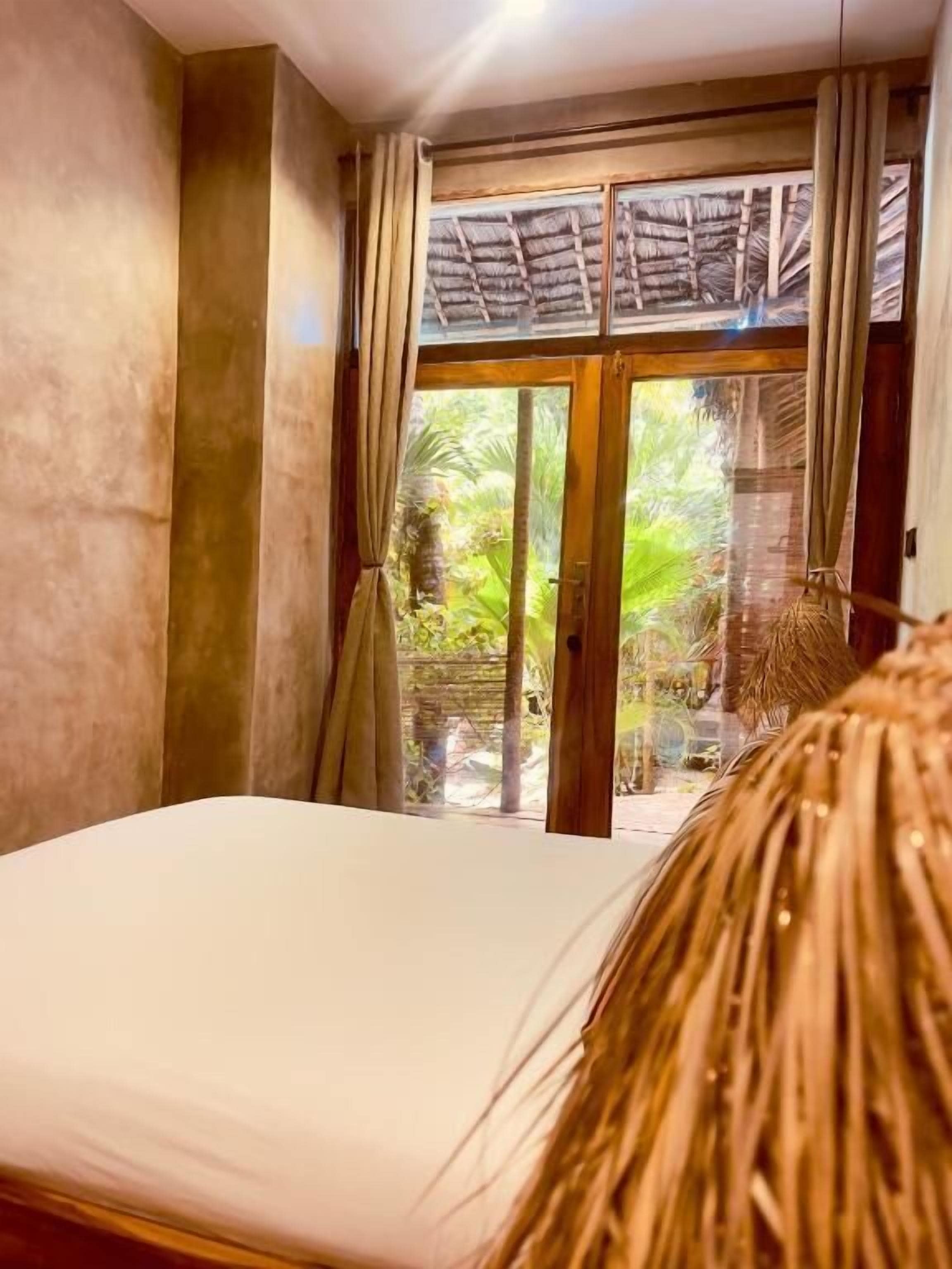Una habitación con cama, cortinas y vistas al verdor exterior.