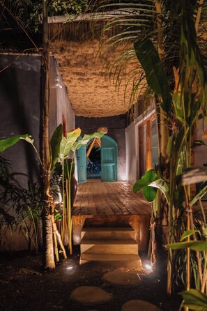 A narrow pathway leading to a room with a thatched roof, surrounded by tropical plants. - THE GARTEN LIVING HOTEL (Paje)