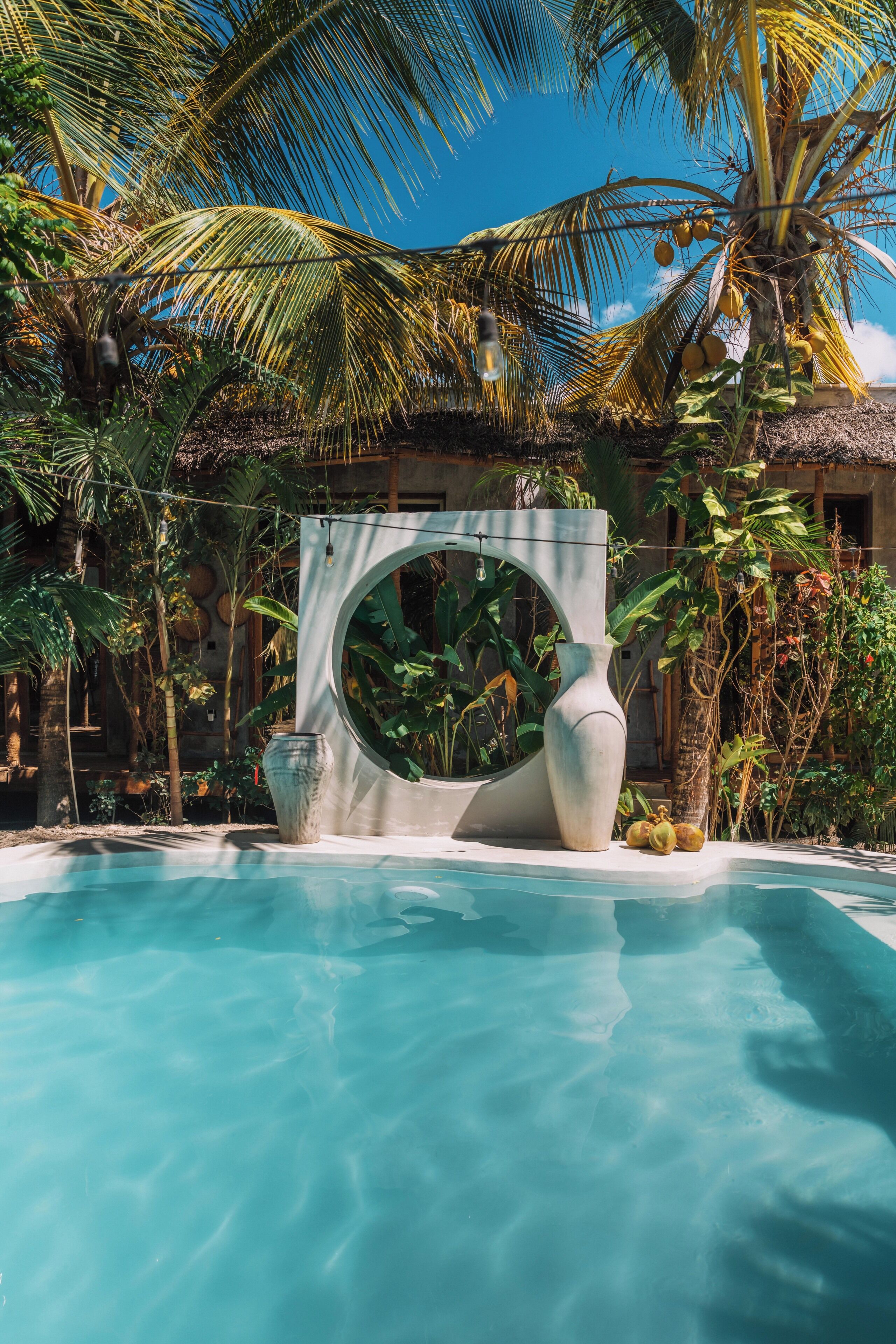 Une piscine d’un bleu éclatant, entourée d’une végétation tropicale et agrémentée d’une grande structure décorative en pierre.