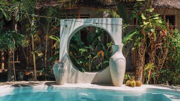 Una piscina azul cristalina rodeada de follaje tropical y una gran estructura de piedra decorativa.