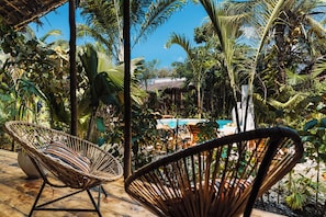 A tropical outdoor area with wicker chairs, a pool, and lush greenery.