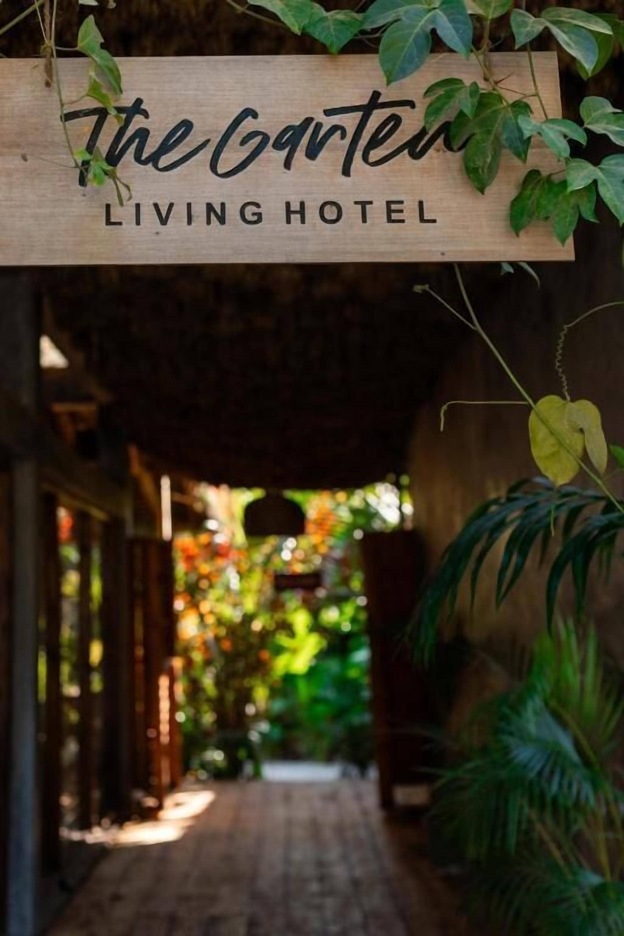 En träskylt med texten ”The Garter Living Hotel”, och en gångväg som leder till ett avskärmat område med växter.
