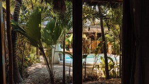 Une terrasse en bois avec une piscine, entourée de plantes tropicales et bordée d’une structure à toit de chaume.