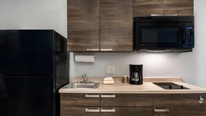 A modern kitchen with dark wood cabinets, a black refrigerator, a microwave, a coffee maker, and a sink.