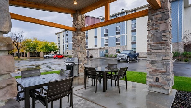 An outdoor patio with stone pillars, a grill, and a table with chairs.
