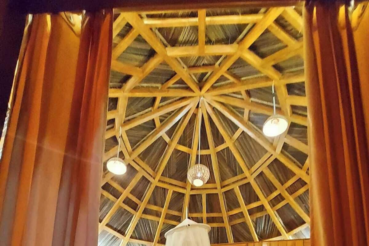 Ett rum med ett högt, geometriskt träpanelat tak, en säng med himmel och träväggar.