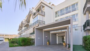 A modern building with a covered entrance, multiple balconies, and a landscaped area with hedges and potted plants. - Apartment 'Sea and Mountain Views' with Sea View, Shared Pool, and AC (Torrox)