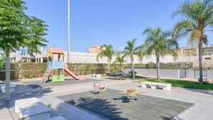 A playground with a slide and climbing structures, surrounded by palm trees and benches. - Apartment 'Sea and Mountain Views' with Sea View, Shared Pool, and AC (Torrox)