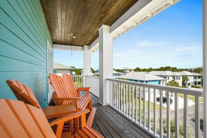 A wooden deck with chairs and a table, overlooking a residential area with houses and a clear sky.