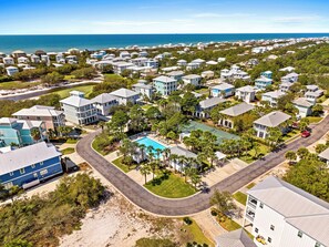 A residential area with houses, a swimming pool, and a beach in the background.