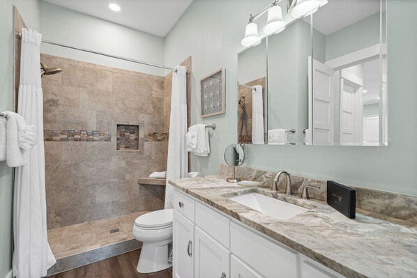 Un baño moderno con ducha, inodoro y lavamanos con un espejo grande.