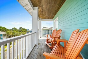 A wooden deck with a railing, two wooden chairs, and a table.