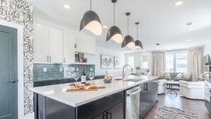 A modern kitchen with a central island, pendant lighting, and a dining area with a sofa and coffee table. - Luxe 4BR Retreat With Rooftop Fire Pit Garage (Nashville)