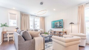 A modern living room with a sofa, armchair, coffee table, and a TV mounted on the wall. - Luxe 4BR Retreat With Rooftop Fire Pit Garage (Nashville)