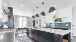 A modern kitchen with dark cabinetry, a large island, pendant lighting, and a view of the city. - Luxe 4BR Retreat With Rooftop Fire Pit Garage (Nashville)