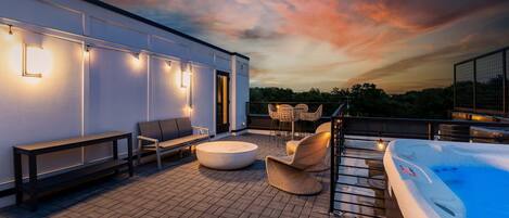 A rooftop patio with a hot tub, seating area, and ambient lighting.