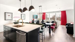 Una cocina moderna con una isla central, comedor con sillas y sala de estar con sofá y cortinas rojas.