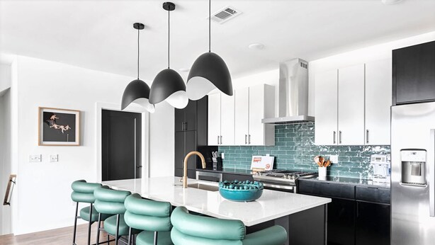 Una cocina moderna con una isla central, taburetes de bar, iluminación colgante y electrodomésticos de acero inoxidable.
