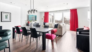 Una sala de estar moderna con comedor, que cuenta con un ventanal grande, cortinas rojas y muebles contemporáneos.