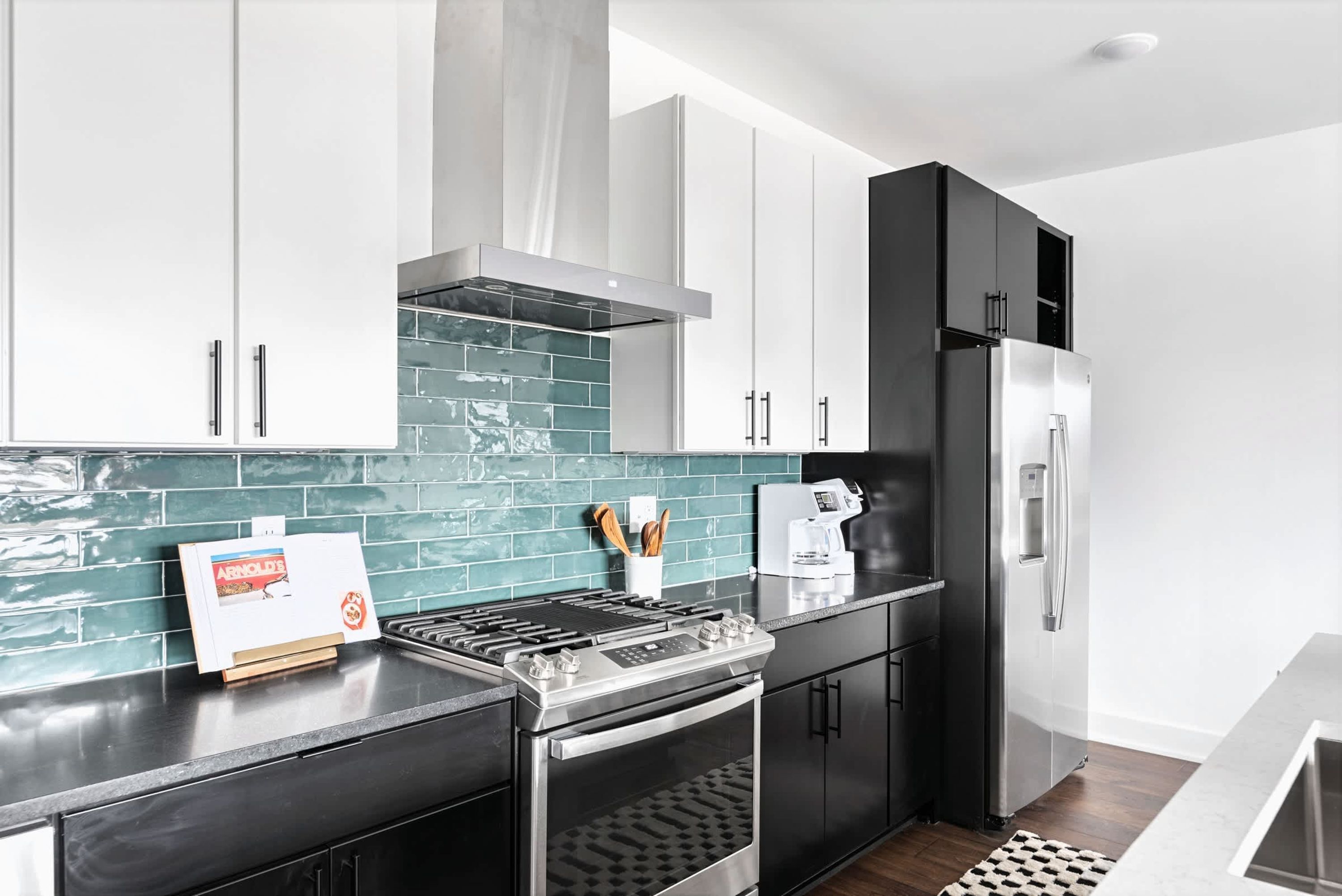 A modern kitchen with a stainless steel stove, black cabinets, and a teal backsplash.