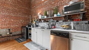 A kitchen with white cabinets, a stainless steel microwave, and a brick wall. - Peaceful and Private Retreat (Lafayette)
