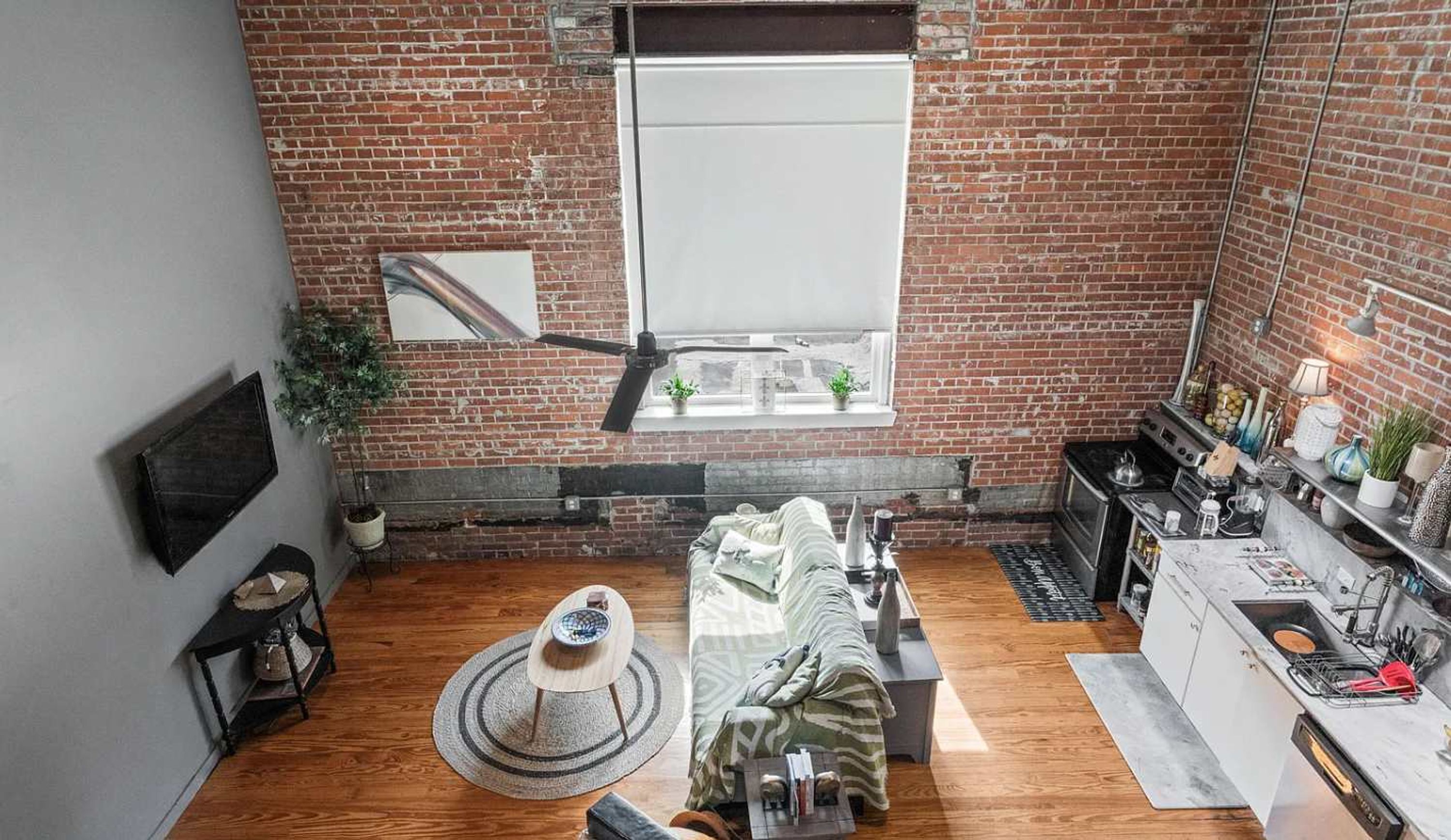Una habitación estilo loft con paredes de ladrillo visto, un ventanal grande, un sofá, un rascador para gatos y una kitchenette.