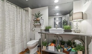 A modern bathroom with a toilet, sink, and mirror. There are plants and a shelf with towels. - Peaceful and Private Retreat (Lafayette)