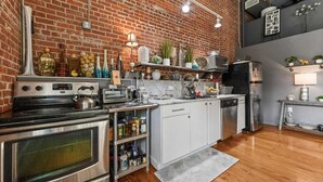 A kitchen with a brick wall, stainless steel appliances, and various kitchen items on shelves. - Peaceful and Private Retreat (Lafayette)