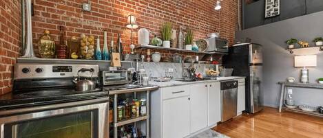 A kitchen with a brick wall, stainless steel appliances, and various kitchen items on shelves.