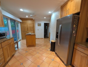 Una cocina con armarios de madera, un refrigerador de acero inoxidable, una isla de madera y piso de baldosas.