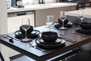 A dining table set with black plates, bowls, and wine glasses, with utensils placed on the table.