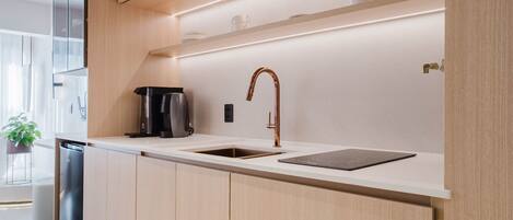A modern kitchen with wooden cabinets, a built-in oven, a coffee maker, and a sink.