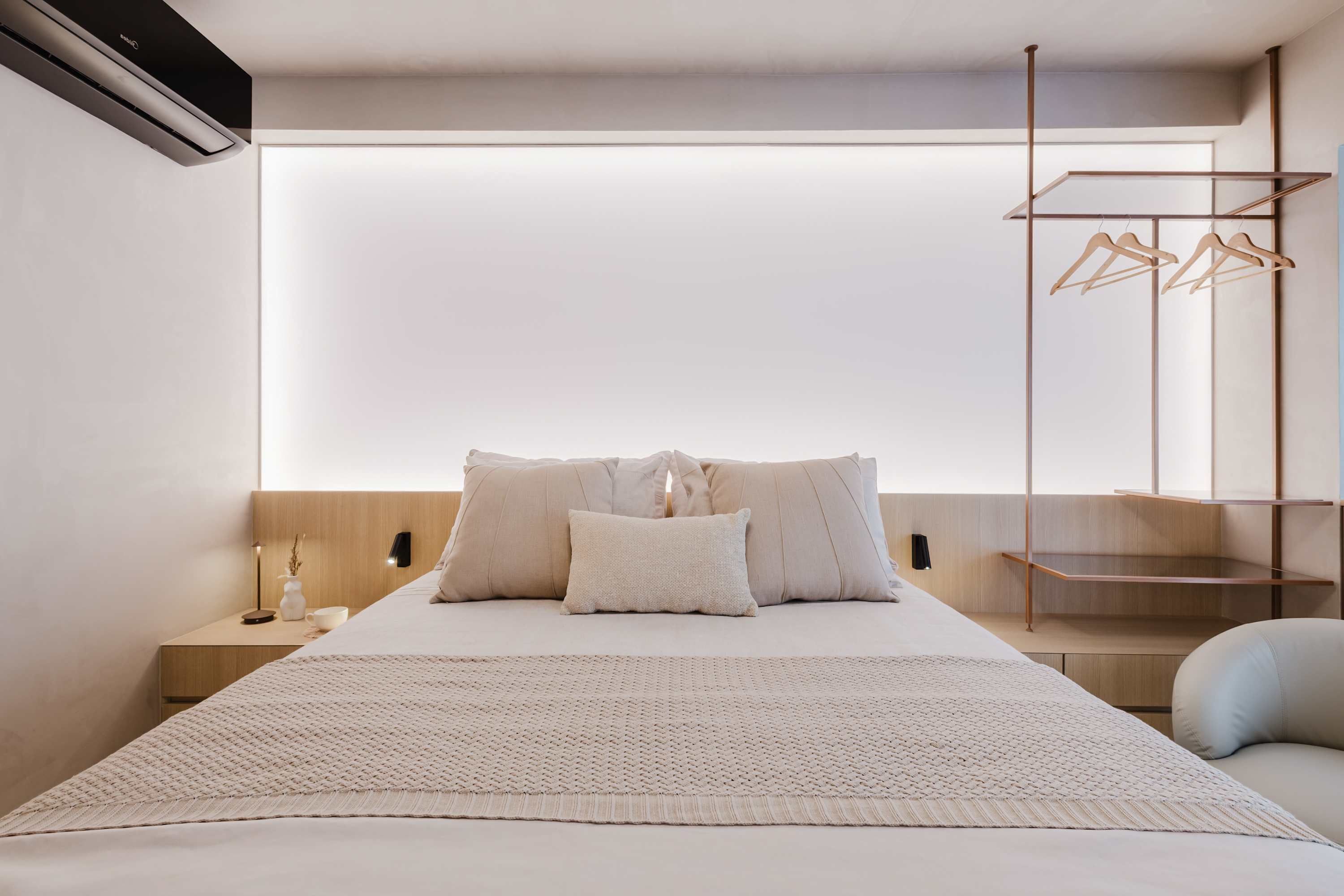 A modern bedroom with a large bed, a bedside table with a lamp, and a wall-mounted drying rack.