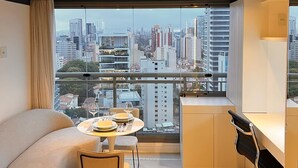 A modern living room with a city view, a round table with chairs, a sofa, and a desk with a chair. - Do Pinheiros I Stylish Studio in Sao Paulo (São Paulo)