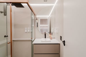 A modern bathroom with a glass shower enclosure, a white sink with a single faucet, and a mirror above the sink.