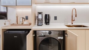 A compact kitchen with integrated appliances, including a dishwasher, washing machine, and coffee maker, with light wood cabinetry and a modern design. - Viana Home Design Studio in Pinheiros (São Paulo)