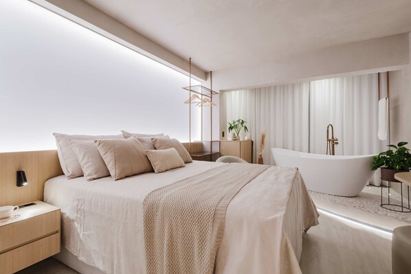 Une chambre à coucher moderne avec un grand lit, une baignoire sur pieds et une table de chevet avec une lampe.