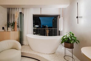 Une salle de bain moderne avec une baignoire sur pieds, un lavabo blanc et une plante en pot.