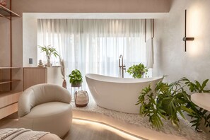 Une salle de bain moderne avec une baignoire sur pieds, un coin salon circulaire et diverses plantes.
