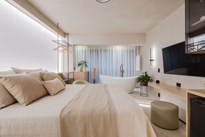 Une chambre à coucher moderne avec un grand lit, une coiffeuse avec un miroir, une baignoire et un téléviseur fixé au mur.