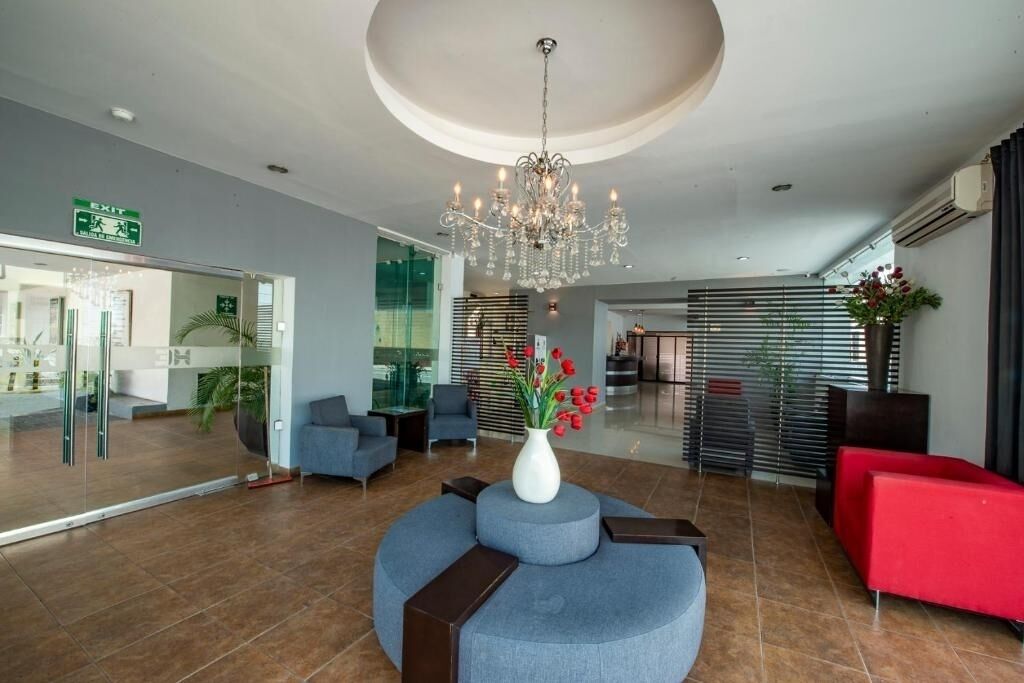 Um lobby moderno com um candelabro, áreas de estar e um balcão de recepção.