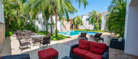 A patio area with outdoor furniture, a swimming pool, and palm trees.