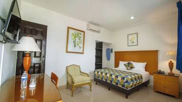 Quarto de hotel com uma cama, uma cadeira, uma mesa com abajur, uma televisão e um ar condicionado.